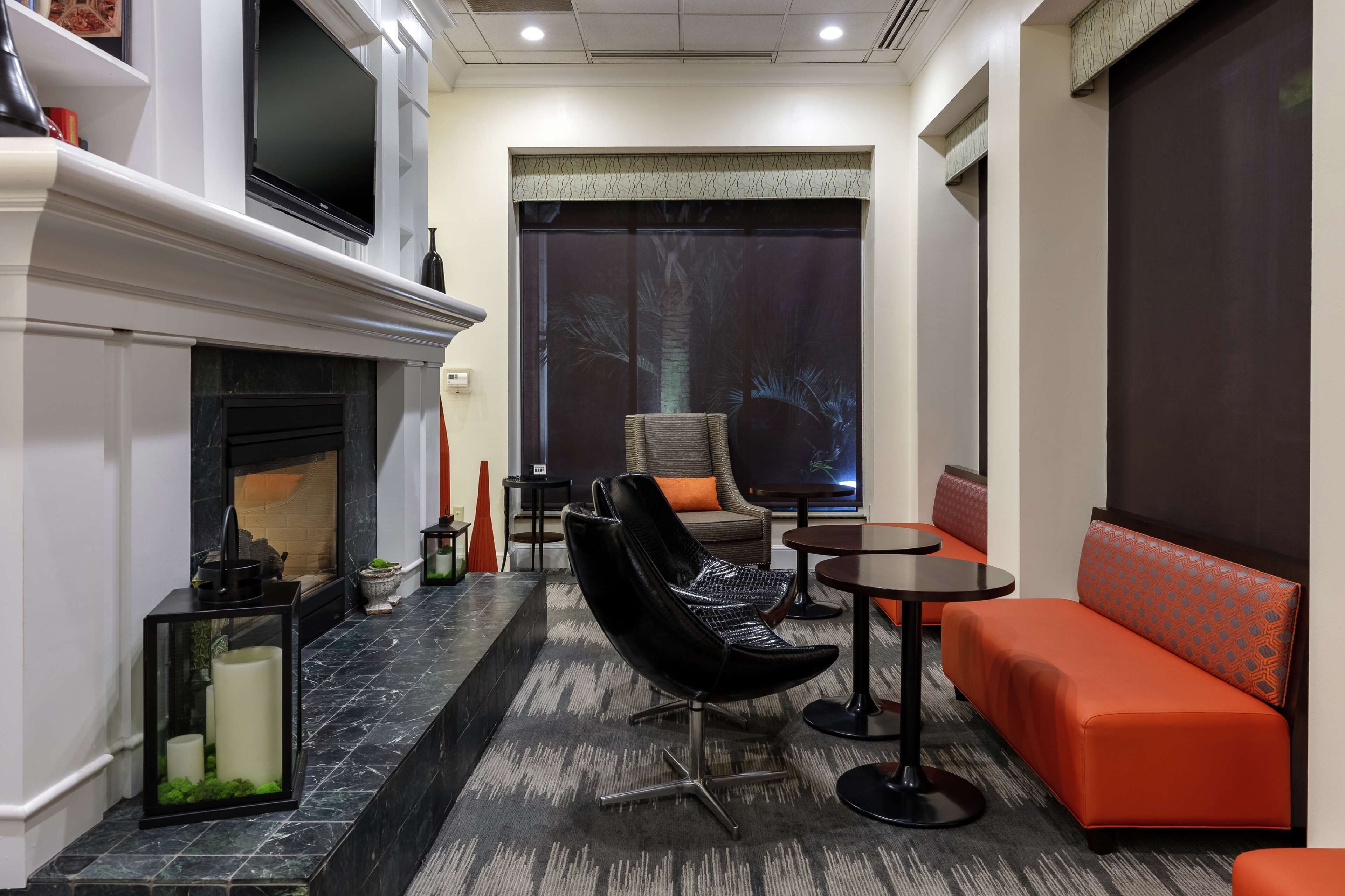 A modern lounge area with a fireplace, seating, and a large window with a view of palm trees.