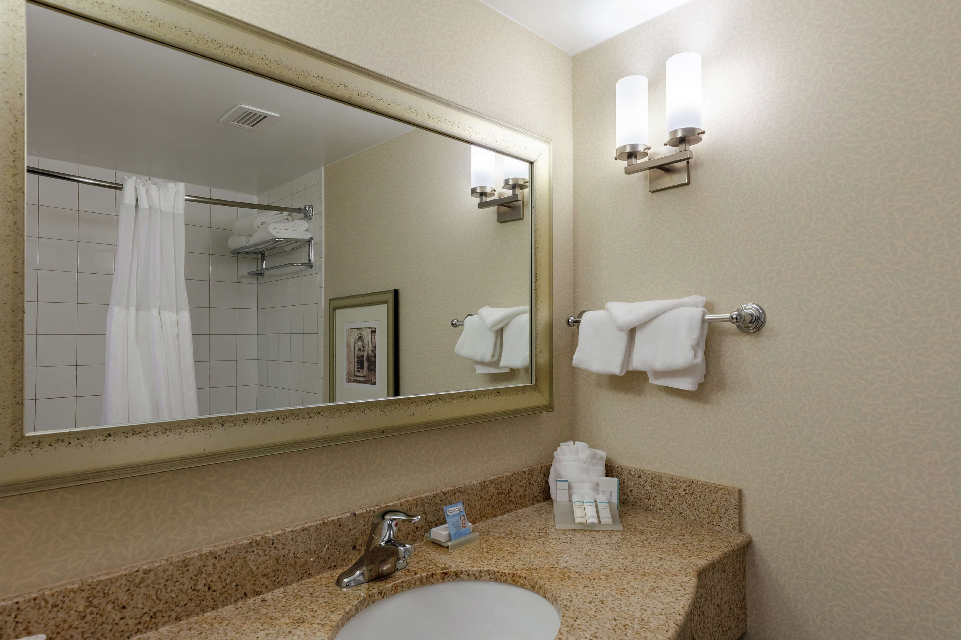 A hotel bathroom with a large mirror, a sink, a shower, and towels on the wall.