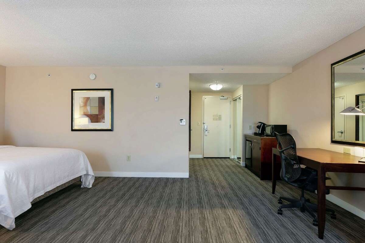 Een hotelkamer met een bed, bureau, stoel en spiegel.