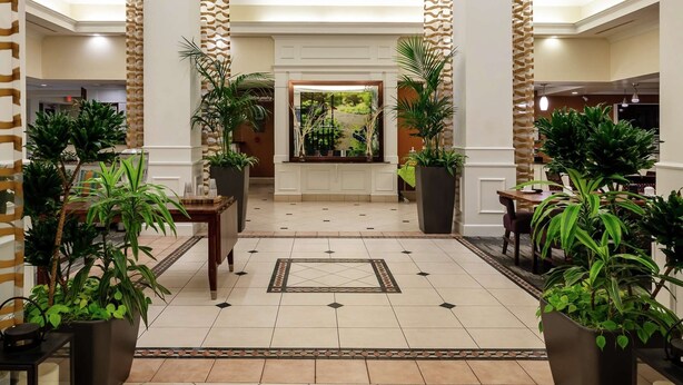 Un hall d’entrée spacieux avec un plafond haut, des colonnes décoratives, des luminaires suspendus et des plantes en pot.
