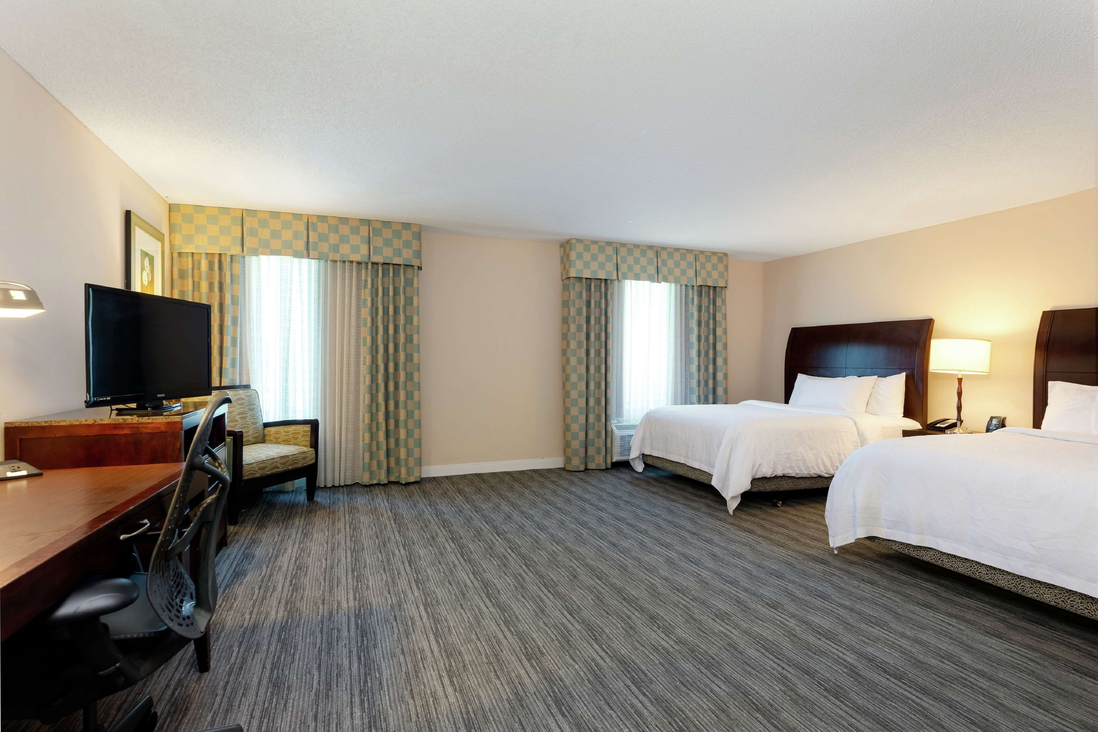 A hotel room with a desk, two beds, a TV, and a lamp.