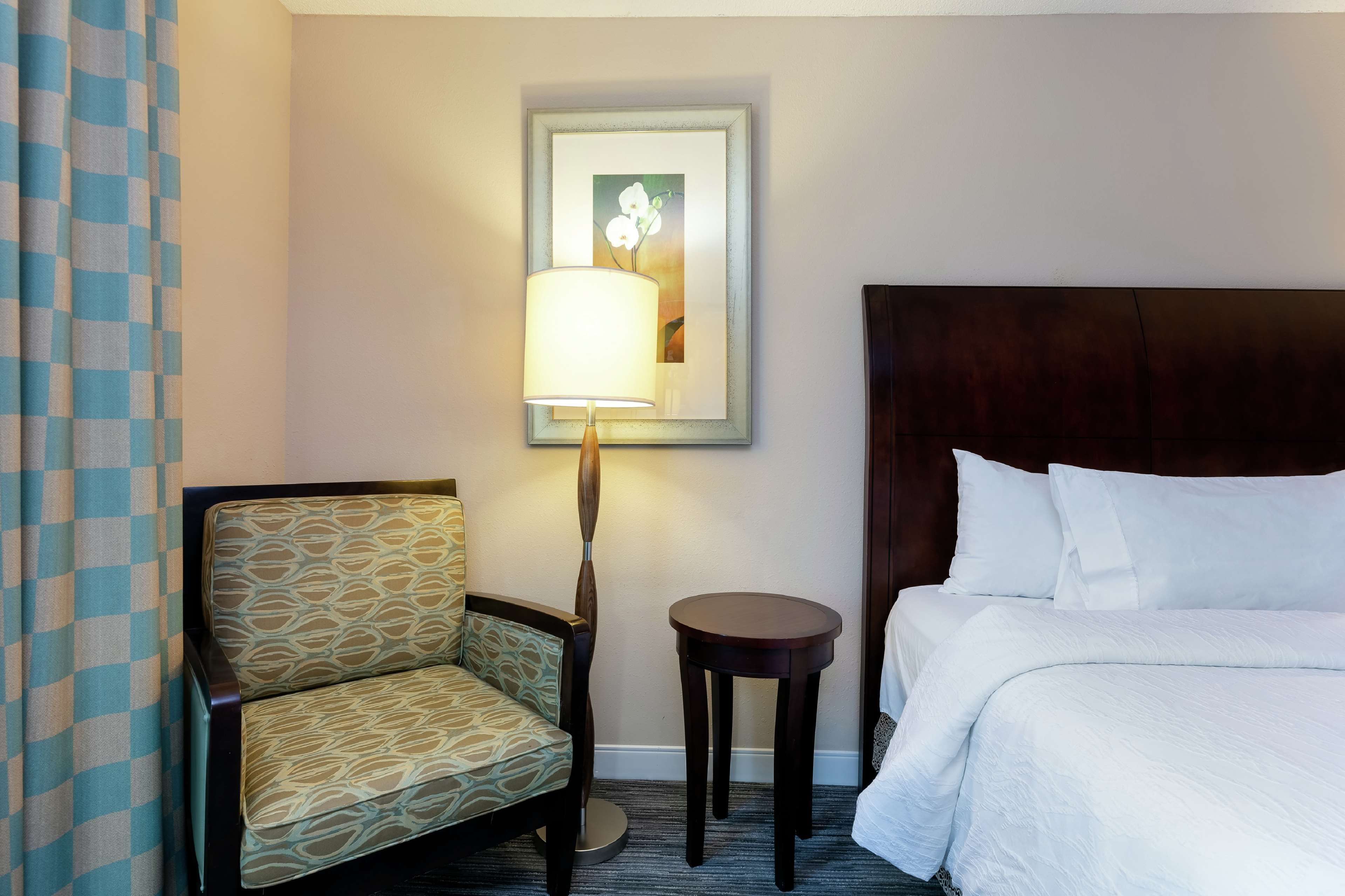 A hotel room with a bed, a chair, a table, and a lamp.