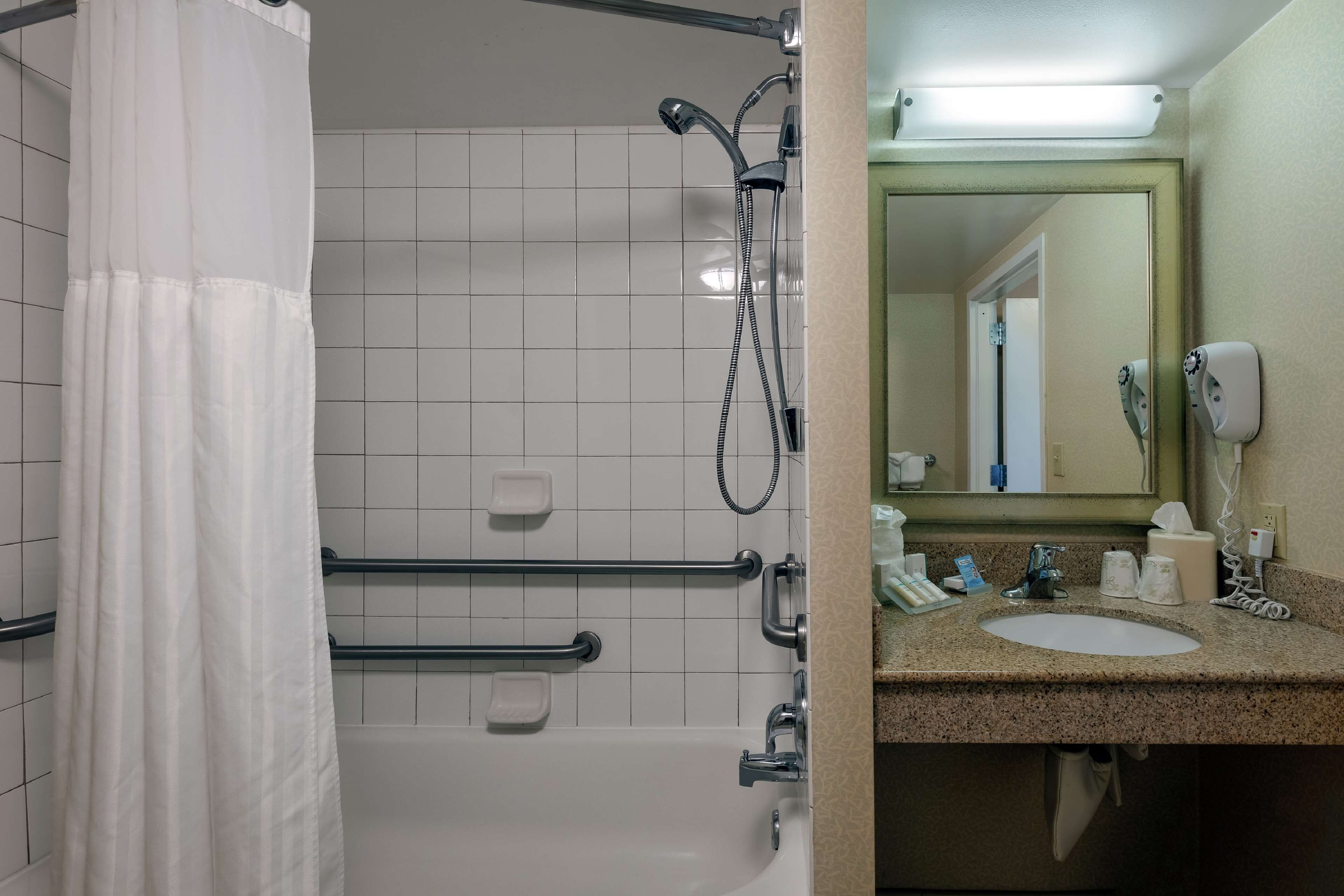 A bathroom with a shower, grab bars, a sink, and a mirror.