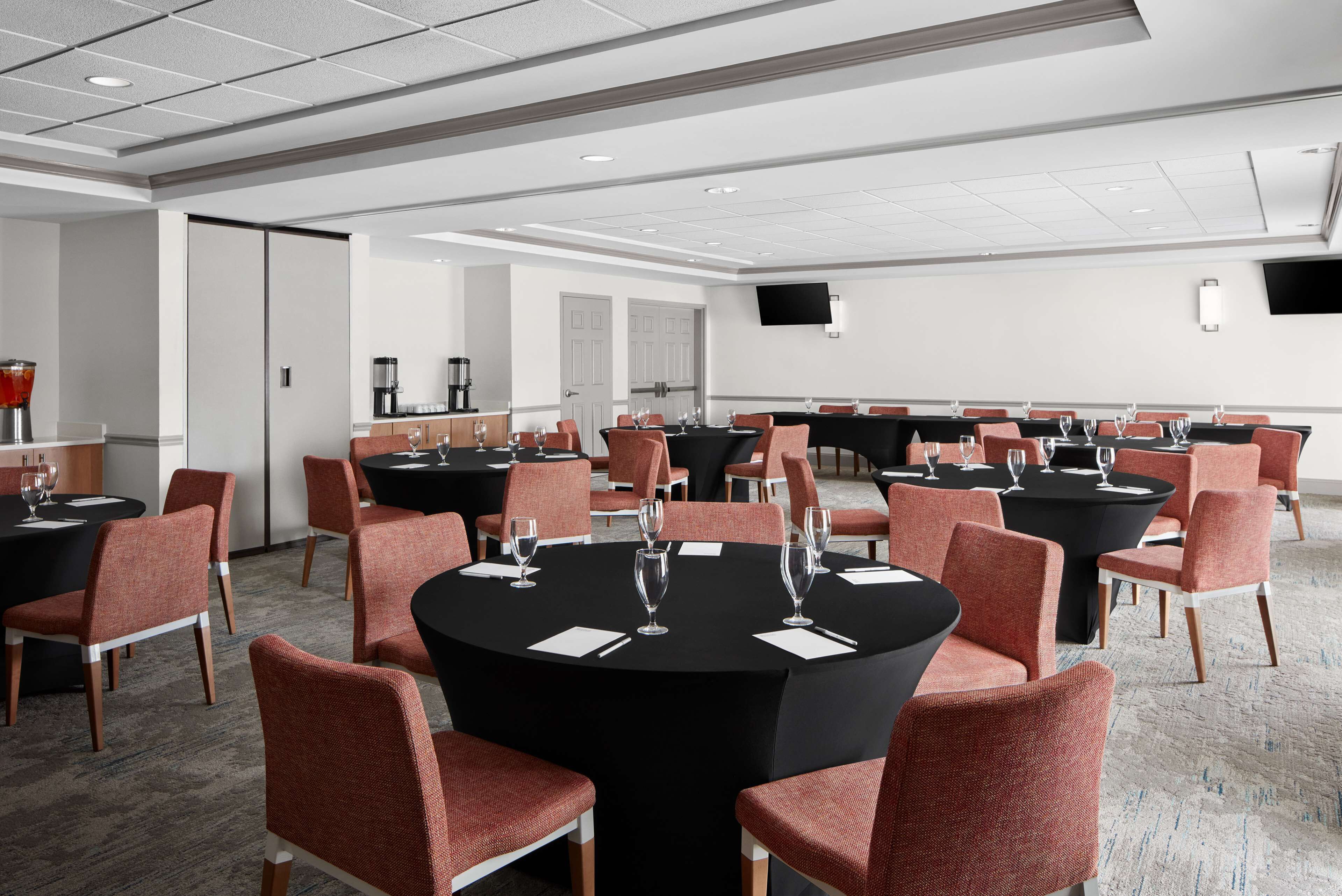 A conference room with round tables, red chairs, and black tablecloths.