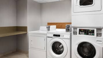 A laundry room with a stacked washer and dryer, a wooden shelf, and a tiled floor.