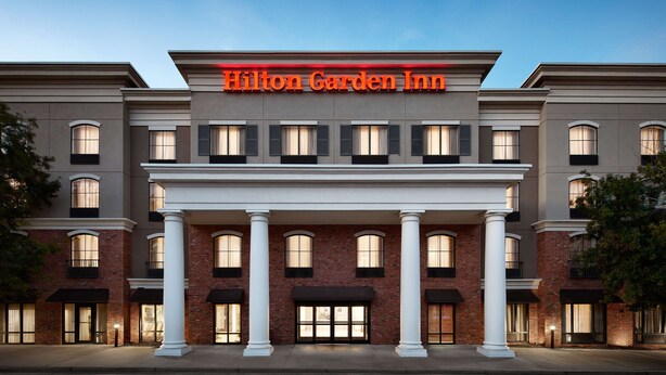 A hotel with a prominent "Hilton Garden Inn" sign, featuring a classic architectural style with brick facade and large windows.