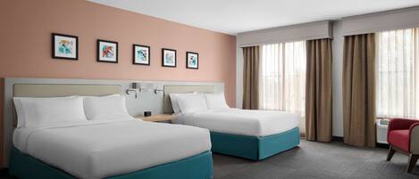 A hotel room with two beds, a desk, a chair, and a window with curtains.