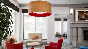 A modern lounge area with a large wooden pendant light, a yellow-striped sofa, red armchairs, and a blue ottoman.
