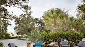 An outdoor patio area with wicker furniture, potted plants, and a view of a building in the background.