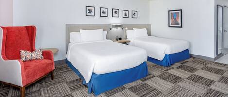 A hotel room with two beds, a red armchair, a nightstand with a lamp, and a framed picture on the wall.