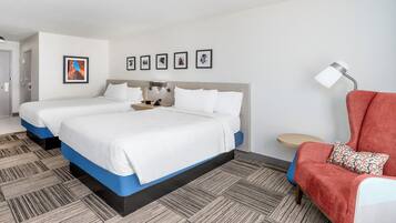 Habitación de hotel con dos camas, un sillón rojo, una mesita redonda y una lámpara de pared.