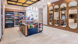 Un espace de vente moderne doté d’un comptoir central où sont exposées des boissons, d’étagères remplies d’en-cas et d’un mur en bois agrémenté de miroirs.