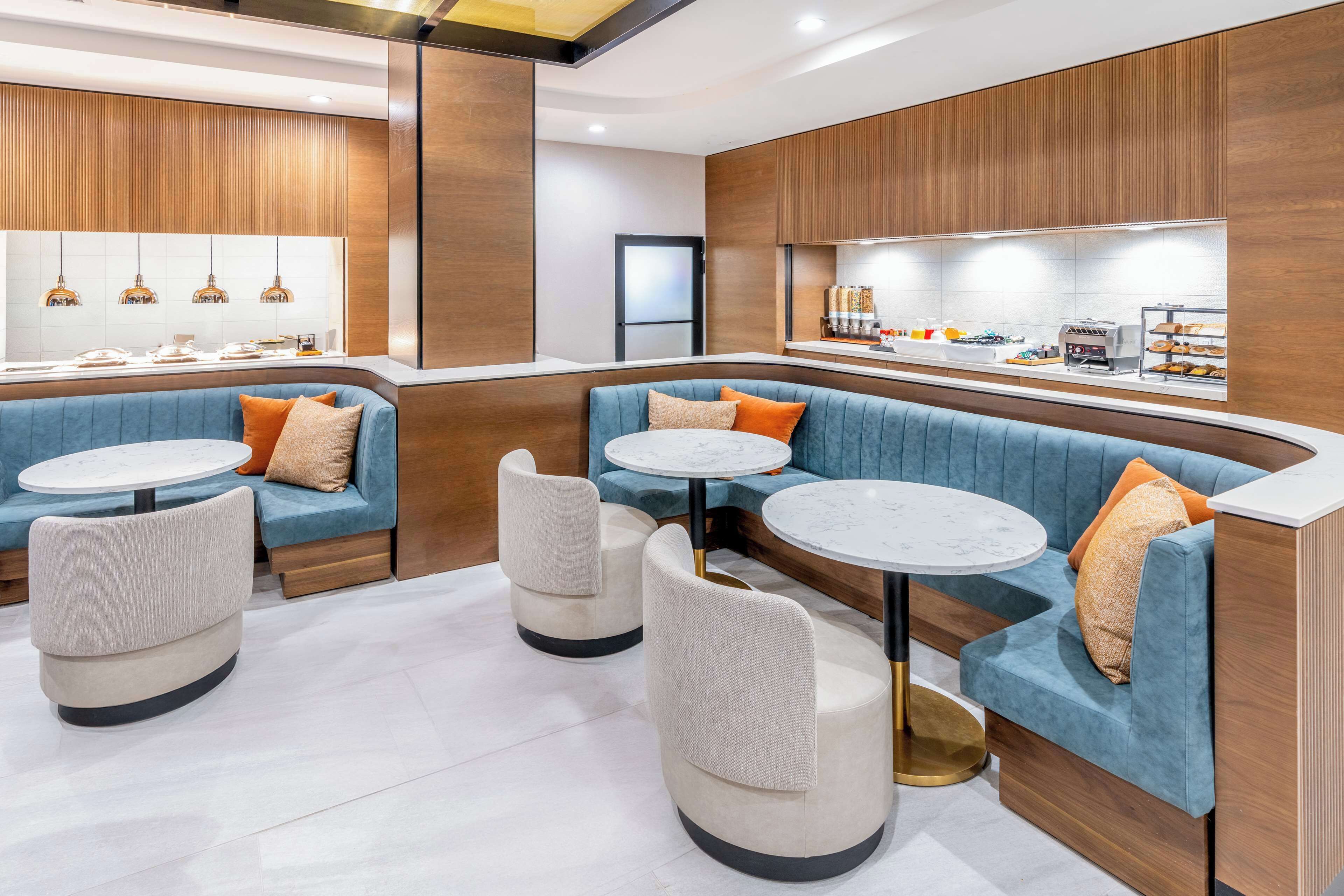 Un restaurant moderne avec des banquettes bleues et des tables rondes, un lambris en bois et un comptoir où sont exposés les plats.