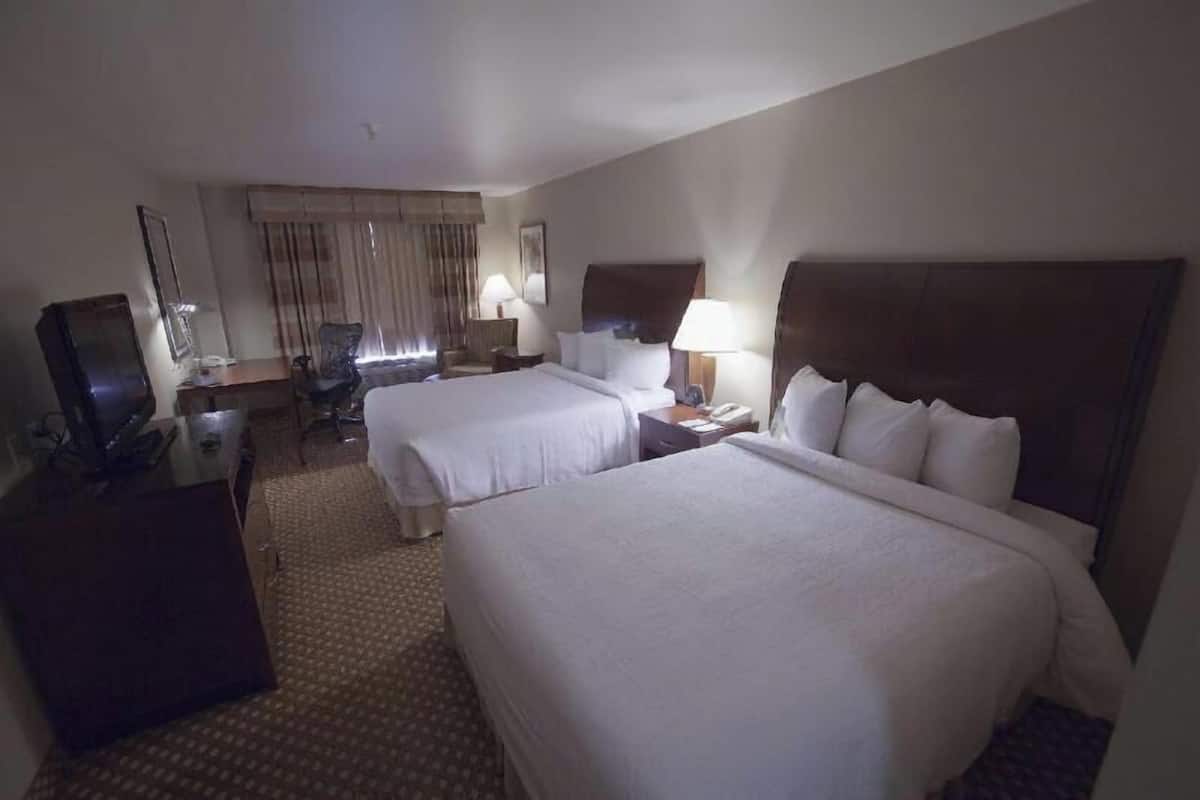 A hotel room with two beds, a desk, a chair, a television, and a window with curtains.