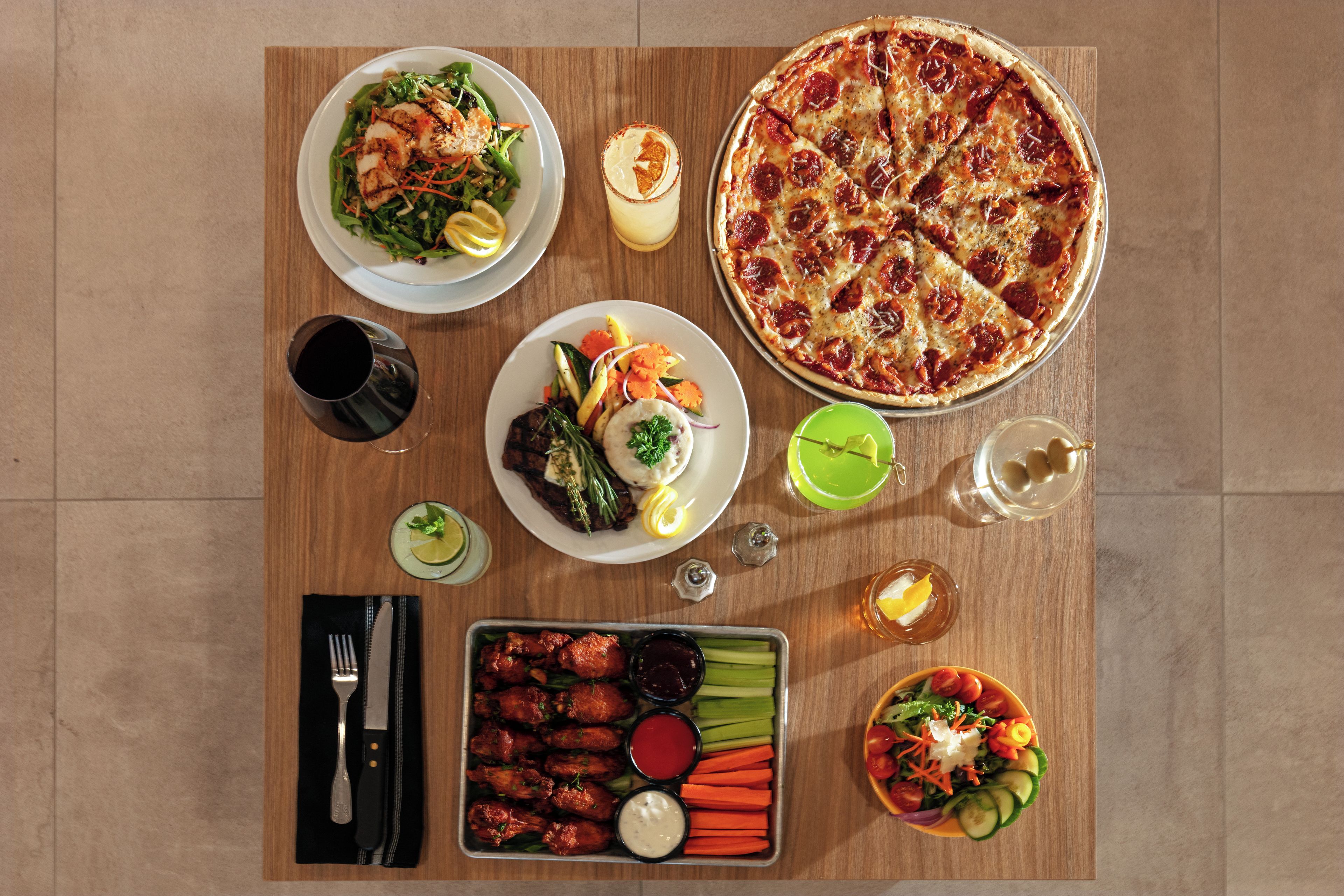 A meal setup with pizza, salads, and wings on a wooden table.