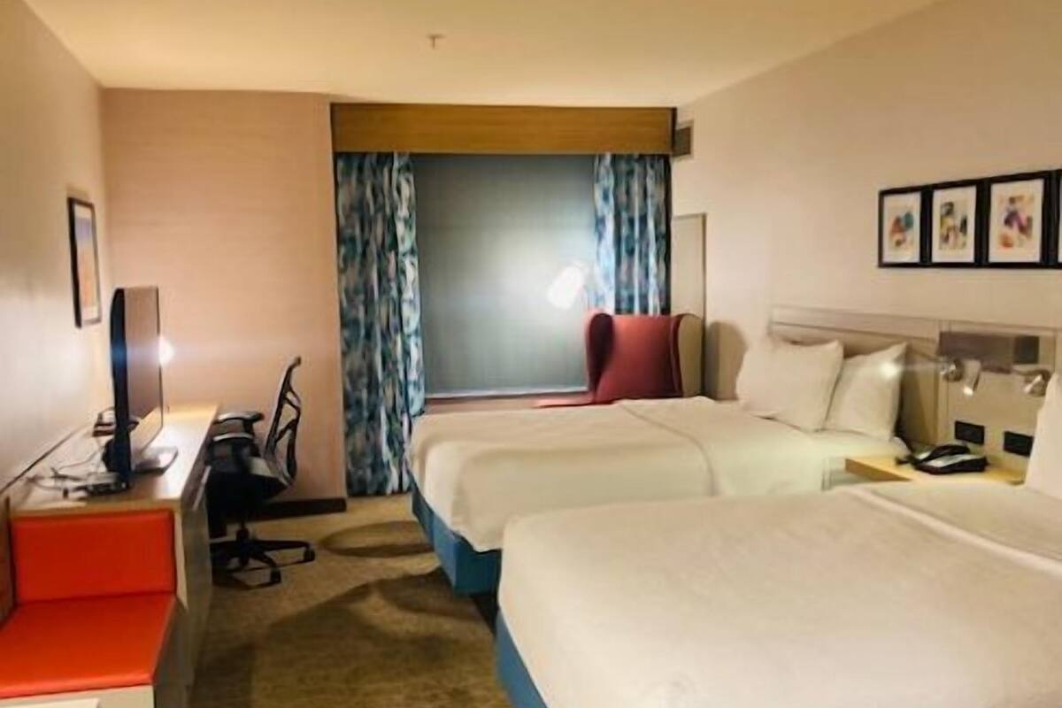 A hotel room with two beds, a desk, a chair, and a window with curtains.