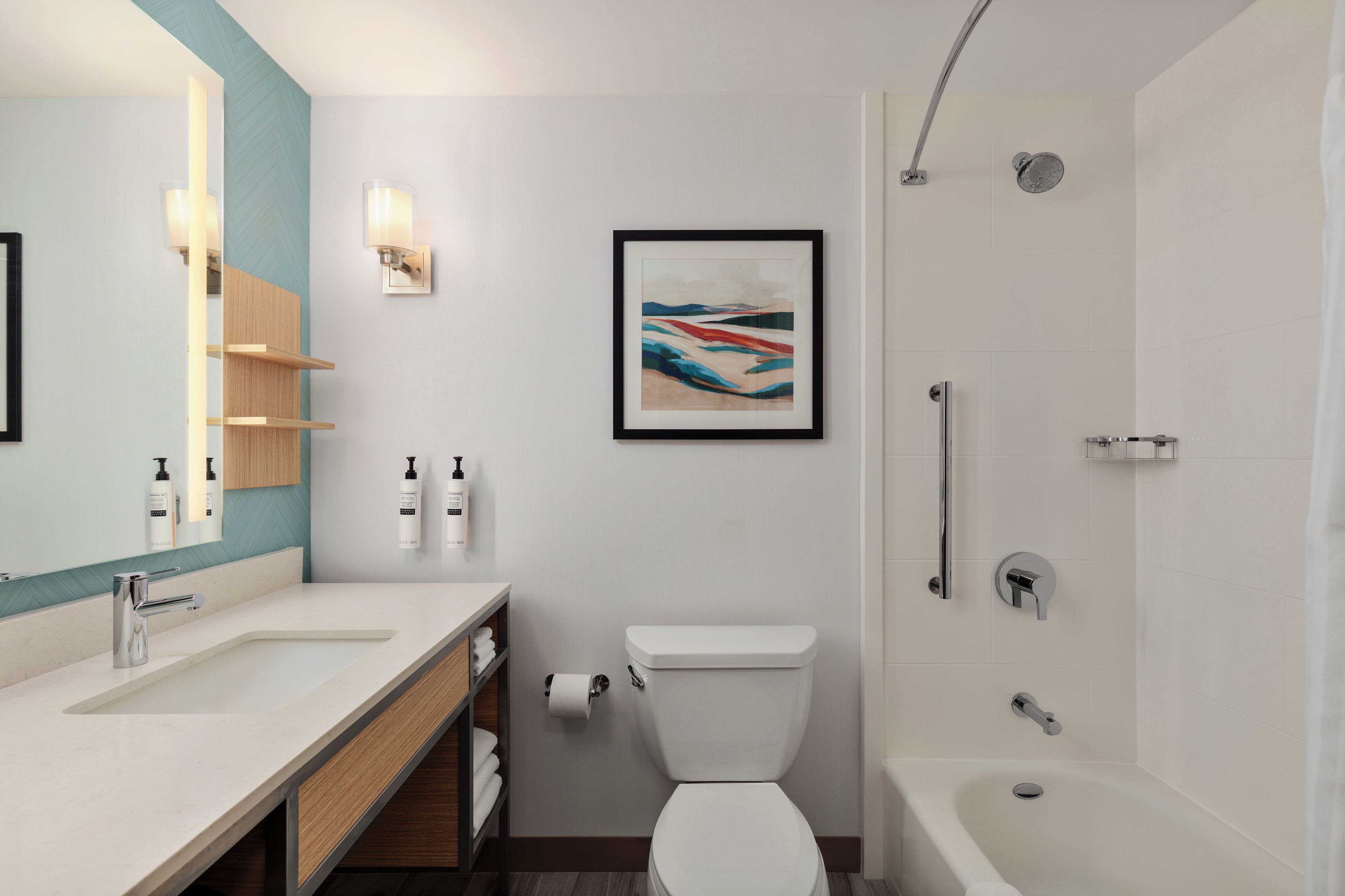 A modern bathroom with a white sink, a toilet, a shower, and a framed abstract painting on the wall.