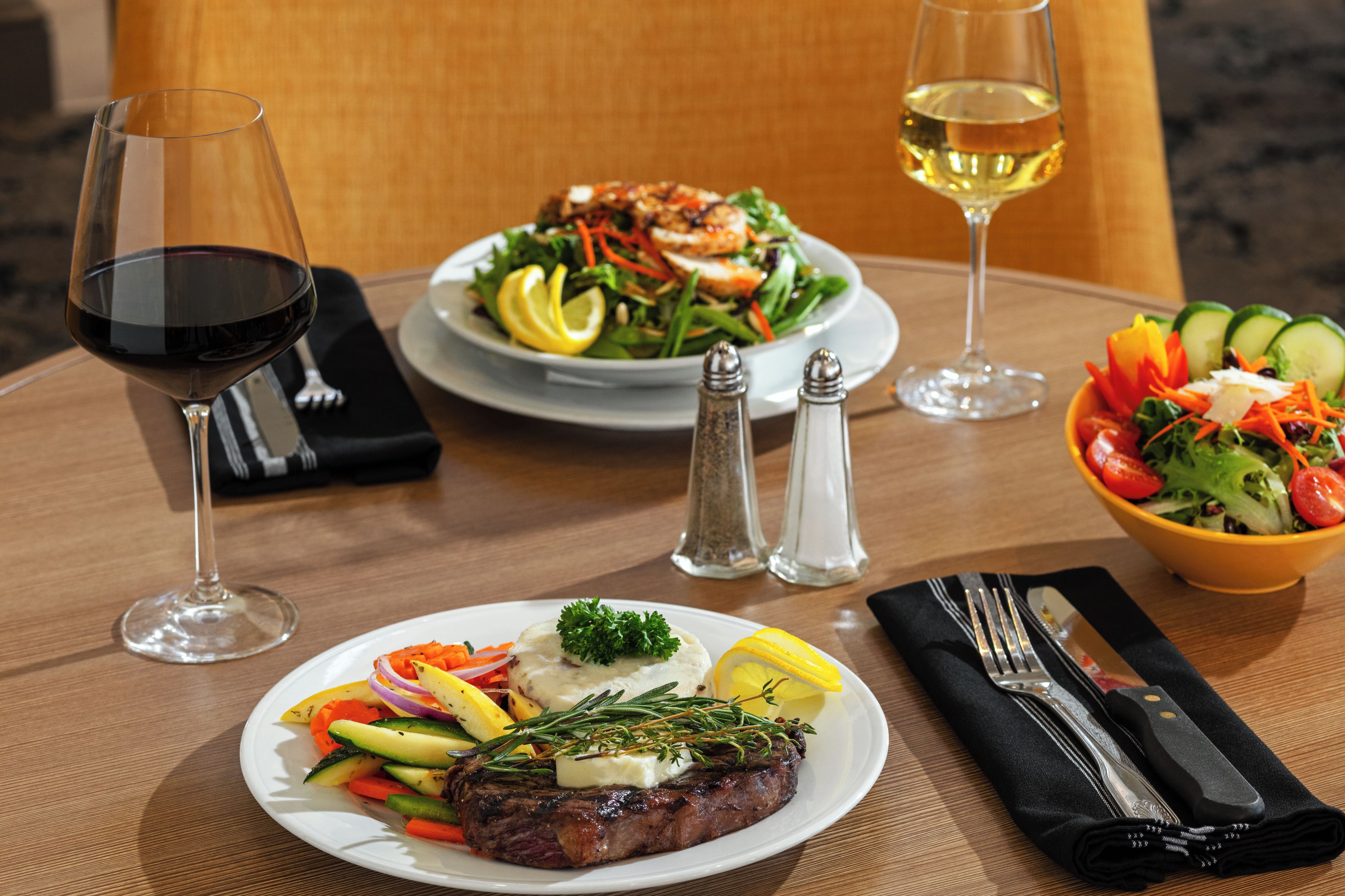 A table set with a steak, salad, and two glasses of wine.