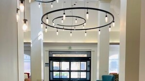 A modern hotel lobby with a central reception desk, circular ceiling lights, and a view of the outside through large glass doors. - Hilton Garden Inn Palmdale (Palmdale)