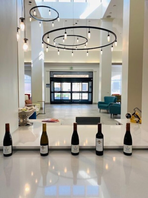 A modern hotel lobby with a central reception desk, circular ceiling lights, and a view of the outside through large glass doors. - Hilton Garden Inn Palmdale (Palmdale)