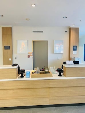 A reception desk with a wooden finish, a door, and framed artwork on the walls. - Hilton Garden Inn Palmdale (Palmdale)