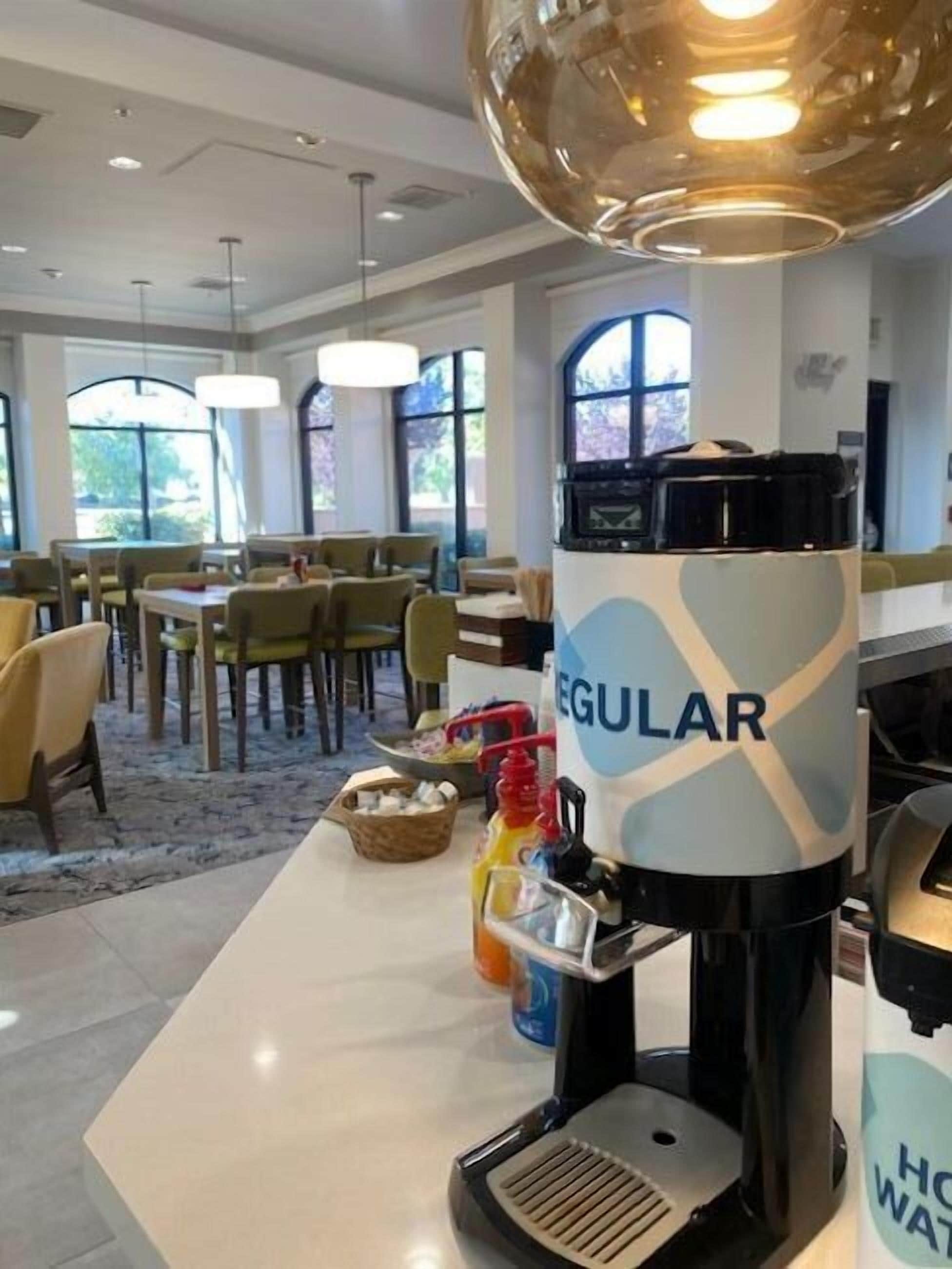 Una estación de café con una máquina de café con marca, zona de estar y ventanas amplias.