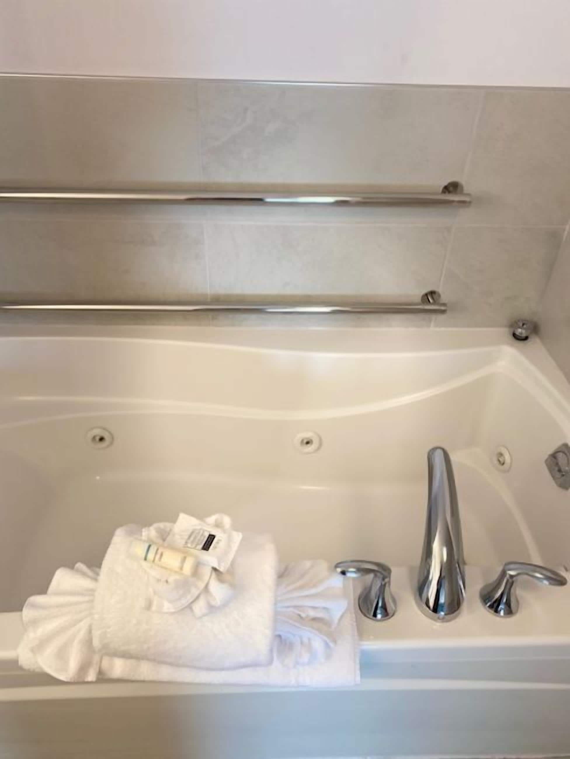 Una bañera con toalla, artículos de tocador, barra de apoyo y ducha.
