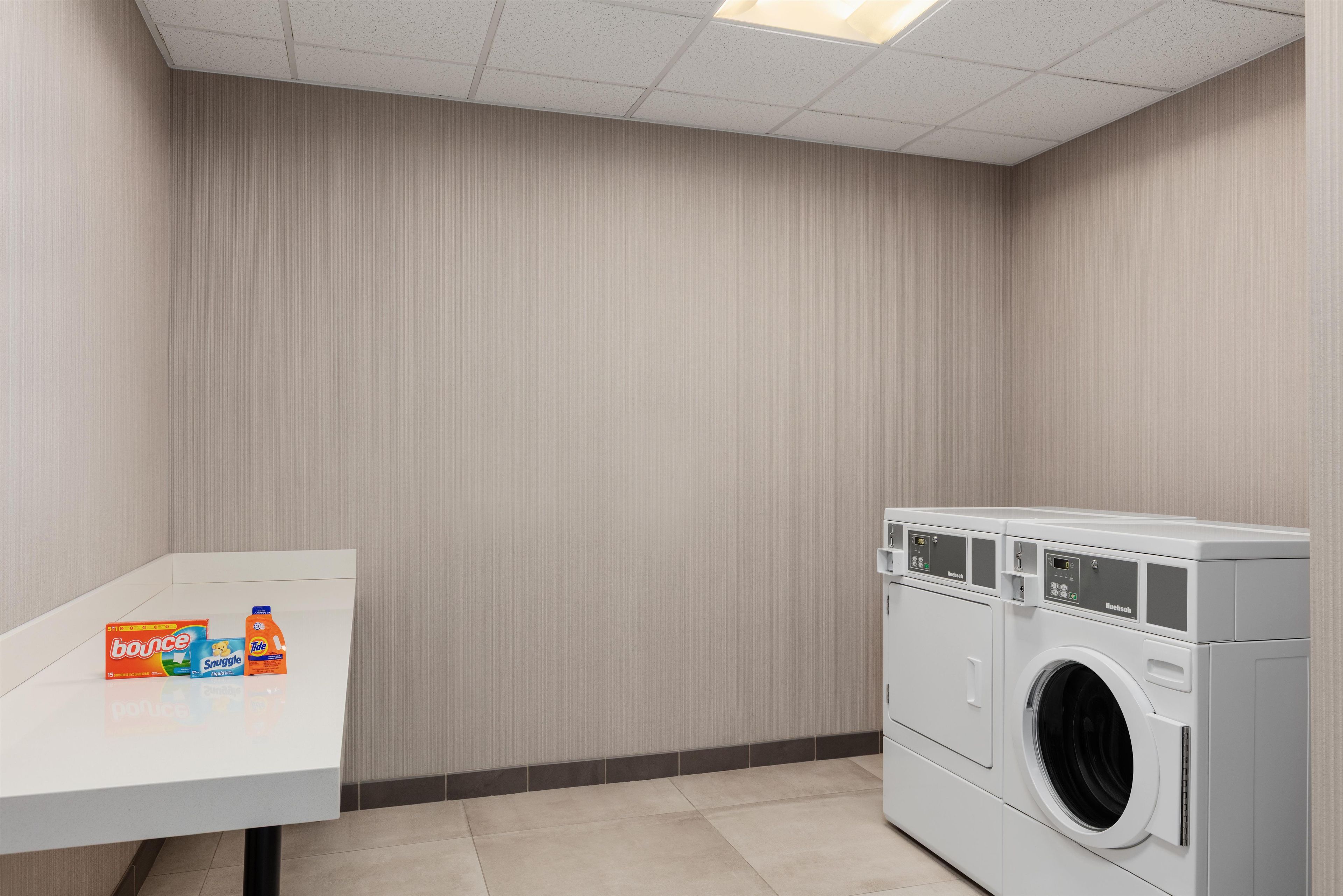 Une buanderie équipée d’un lave-linge et d’une table sur laquelle sont posées des bouteilles de lessive.