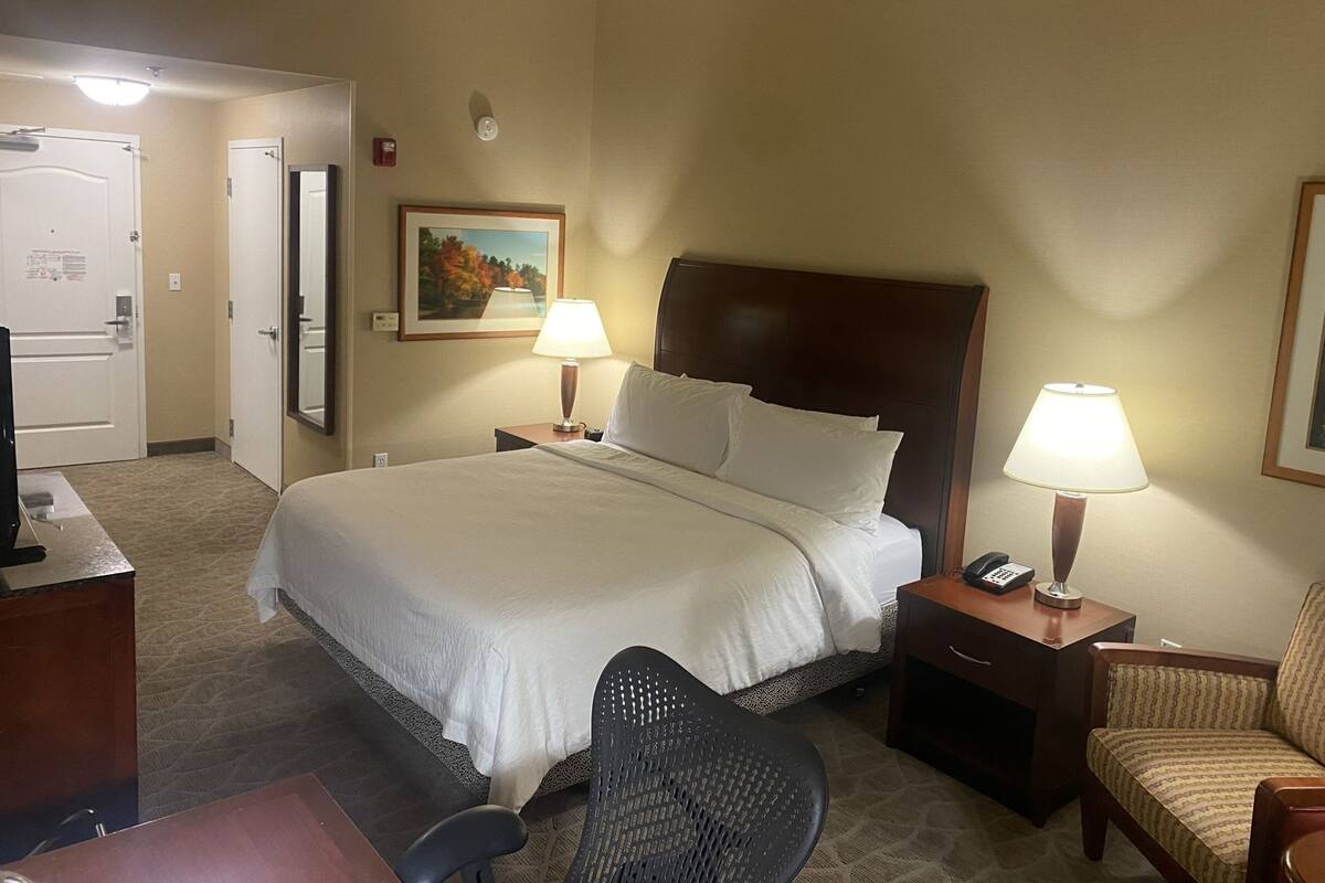 A hotel room with a large bed, two bedside lamps, a desk with a telephone, a chair, and a painting on the wall.