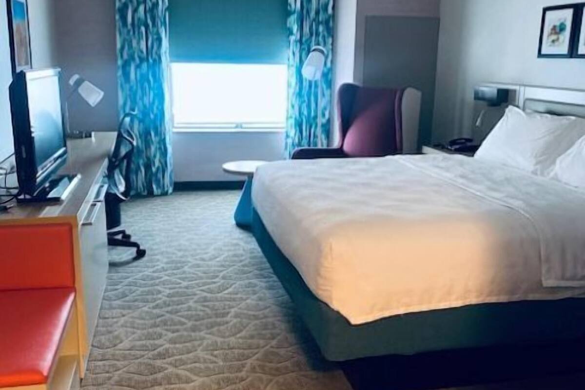 Una camera d'albergo con un letto, una scrivania con un computer, una sedia, un tavolino e una finestra con tende.