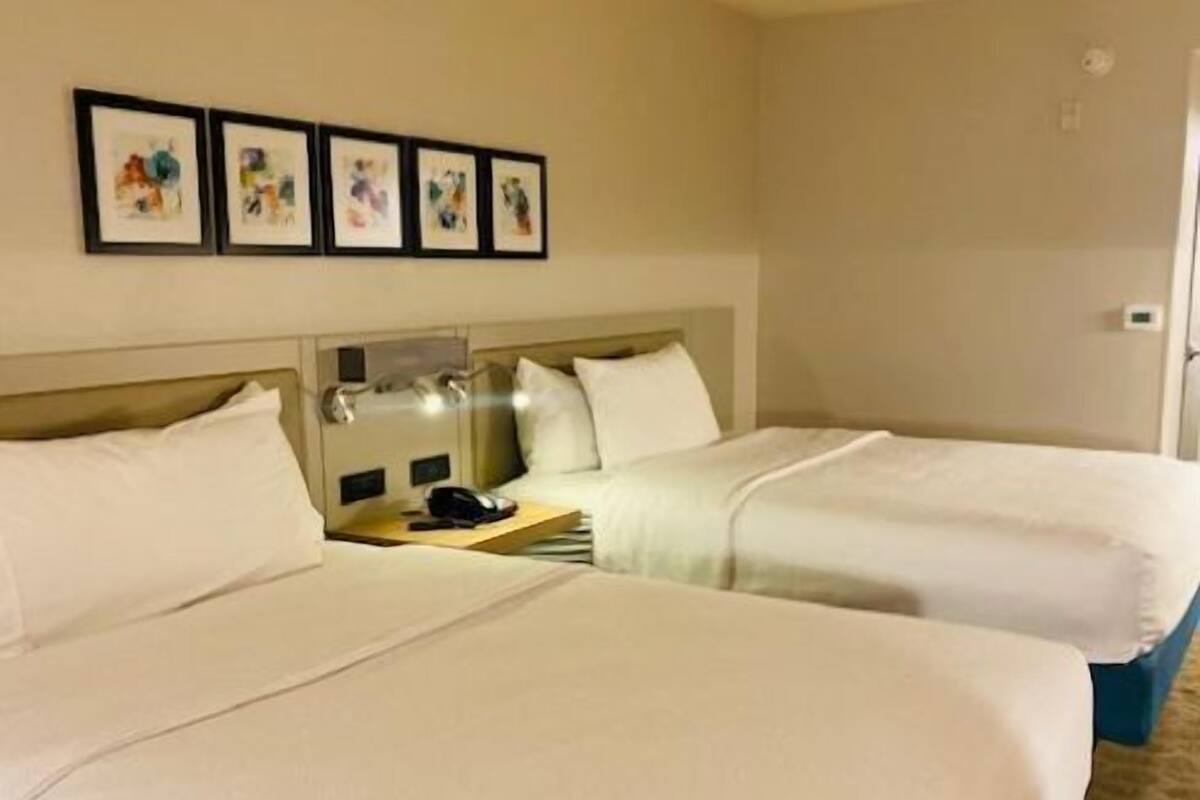 Camera d'albergo con due letti, un comodino con lampada e un'opera d'arte appesa al muro.