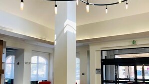 A spacious lobby with a modern design, featuring a central column, seating areas, and a revolving door. - Hilton Garden Inn Palmdale (Palmdale)