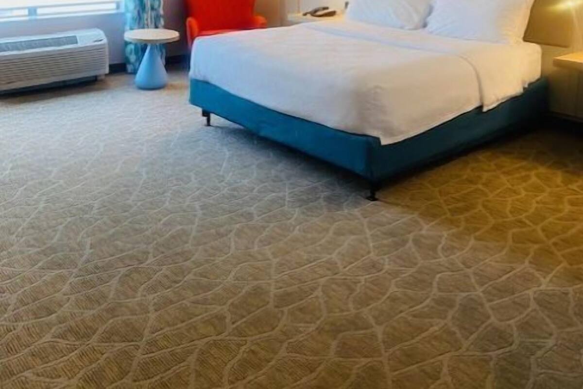 A hotel room with a large bed, a chair, a small table, and a window with curtains.