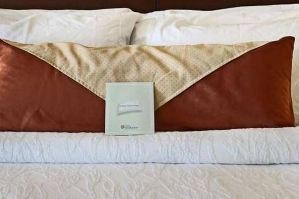 Un letto con biancheria da letto bianca e due cuscini, uno marrone e uno beige.