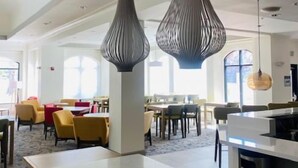 A spacious hotel lobby with modern pendant lighting, a central island, and a view of the dining area. - Hilton Garden Inn Palmdale (Palmdale)
