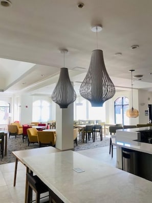 A spacious hotel lobby with modern pendant lighting, a central island, and a view of the dining area.