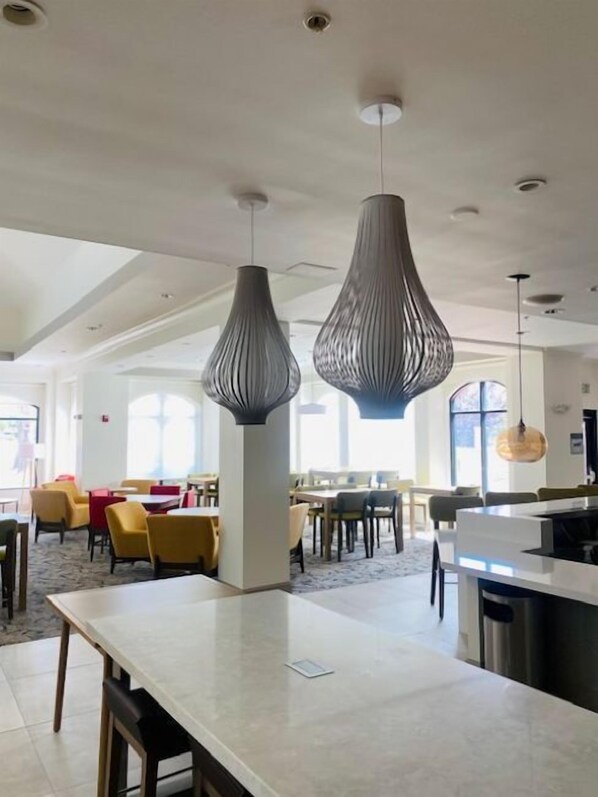 A spacious hotel lobby with modern pendant lighting, a central island, and a view of the dining area. - Hilton Garden Inn Palmdale (Palmdale)
