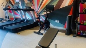 A gym with treadmills, a bench, and a colorful wall.
