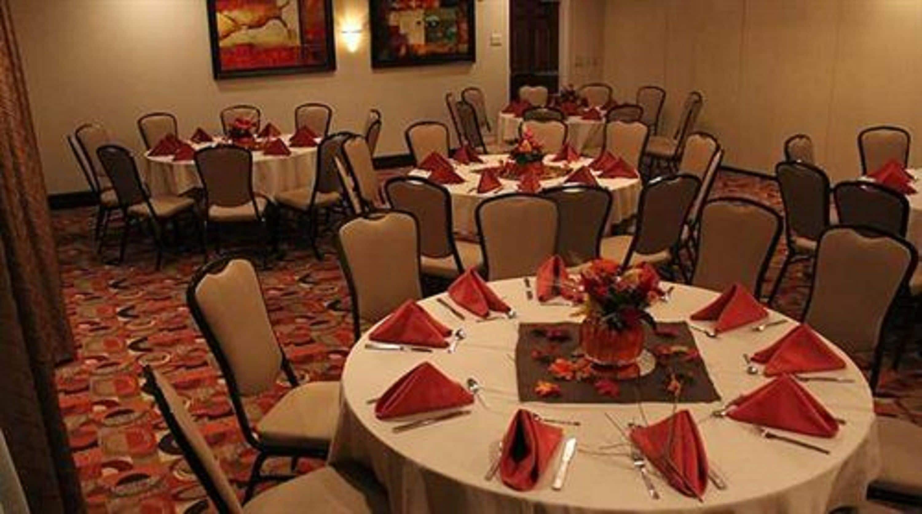 A conference room with multiple round tables, each set with red napkins and silverware, and chairs arranged around them.