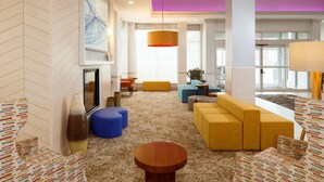 A modern living room with a sofa, ottomans, a coffee table, and a fireplace. - Hilton Garden Inn Cincinnati Blue Ash (Cincinnati)