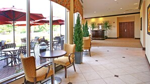 A hotel lobby with a tiled floor, round tables, wicker chairs, and red umbrellas. - Hilton Garden Inn Cincinnati Blue Ash (Cincinnati)