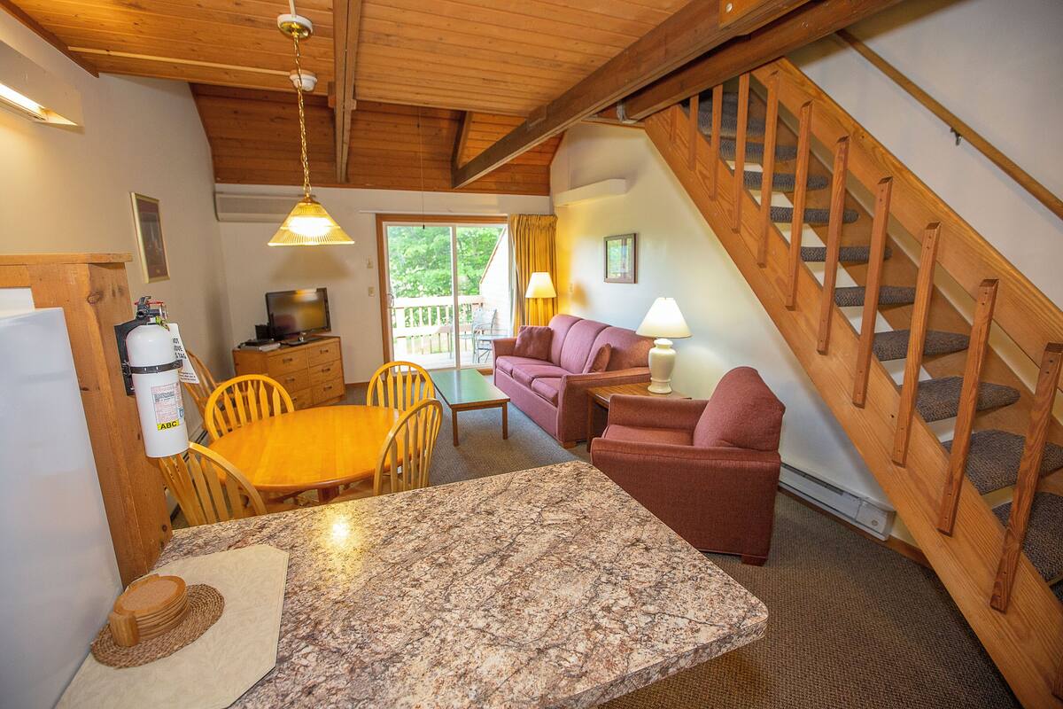 A cozy interior with a wooden staircase, a dining area with a marble table, and a living room with a sofa and lamps.
