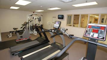 Un gimnasio con cintas de correr, máquinas de pesas y una pantalla digital.