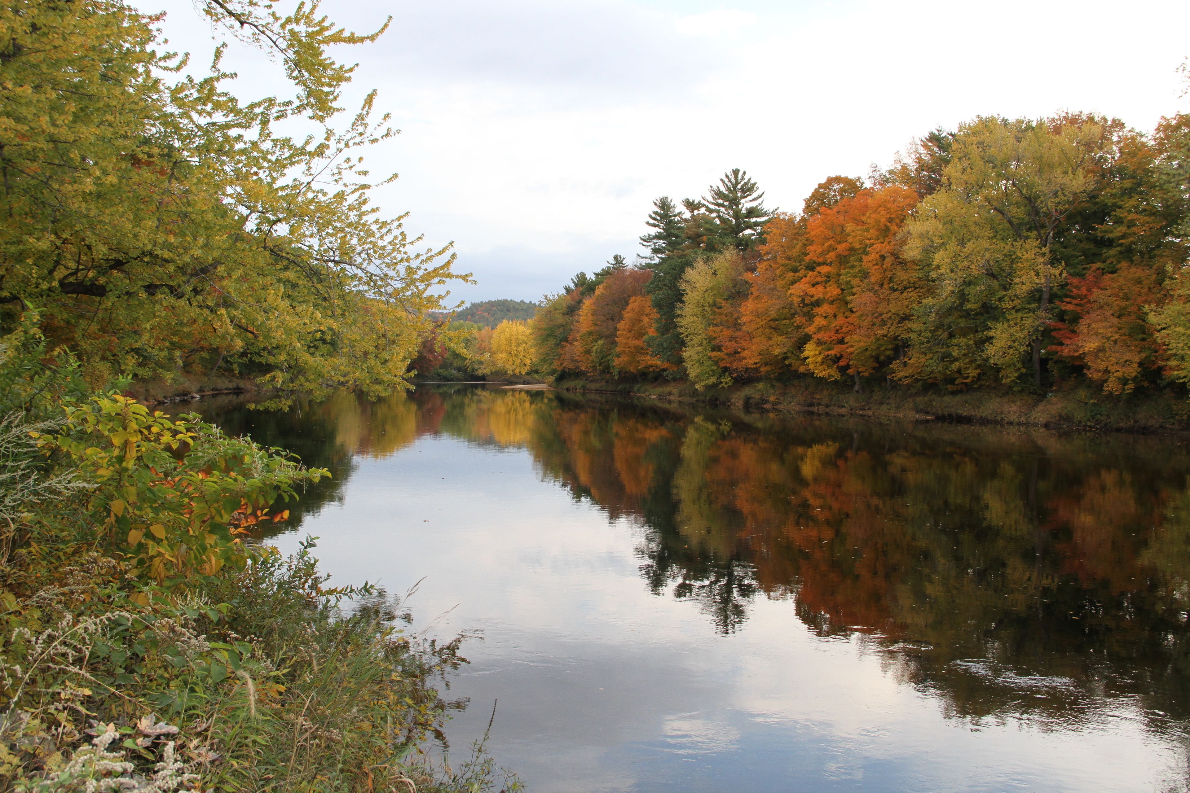 A calm river with autumn foliage reflecting on the water.