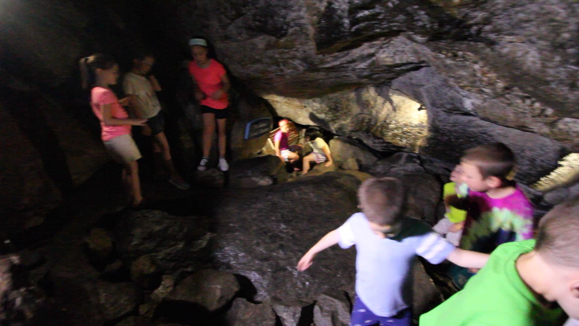 A group of people inside a cave with rocky walls and a small opening at the end.