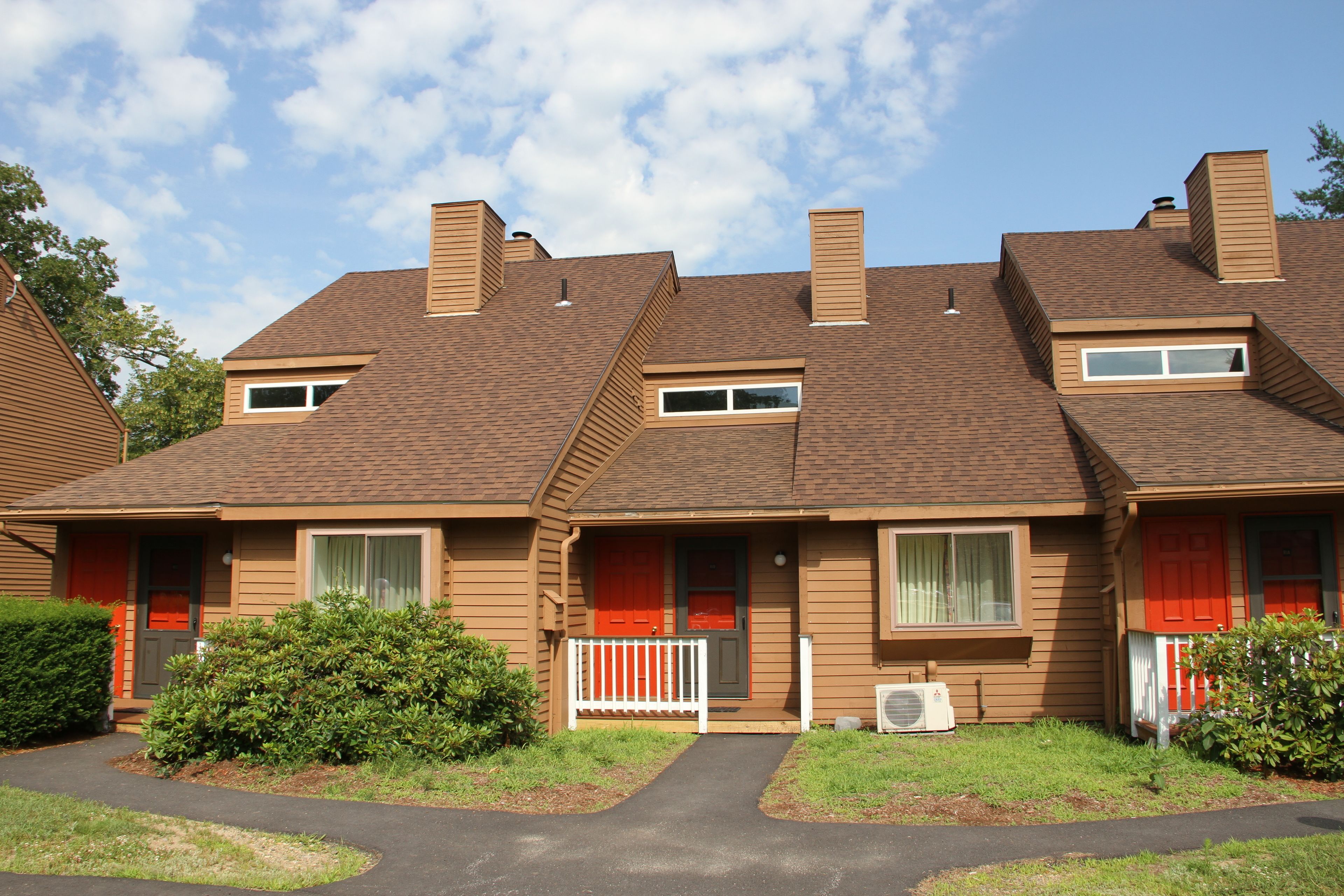 A row of two-story houses with a central walkway, each with a small front porch and a window.
