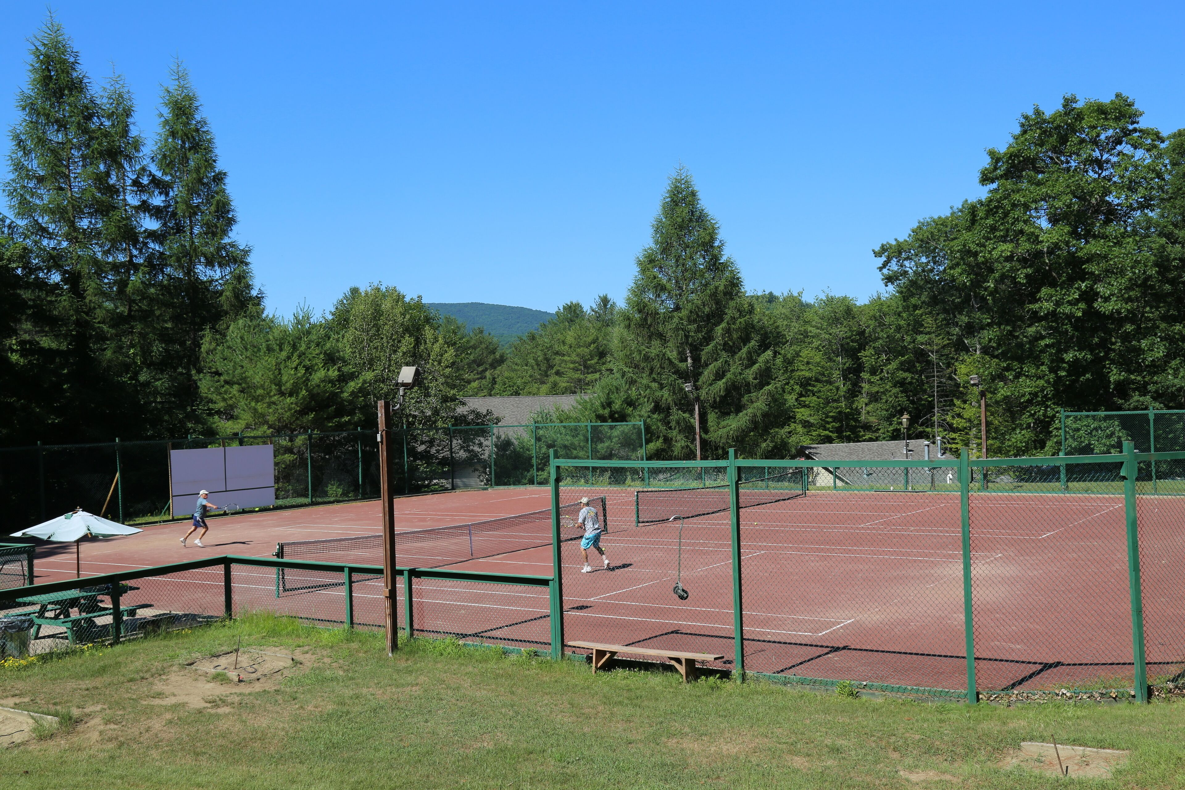 Cancha de tenis con red, rodeada de árboles y una mesa de picnic.
