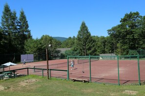 A tennis court with a net, surrounded by trees and a picnic table.