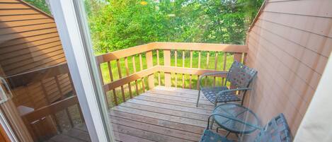 A wooden deck with metal chairs and a glass table.