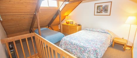 A bedroom with a wooden ceiling, a bed with floral bedding, a nightstand, a lamp, and a framed picture on the wall.